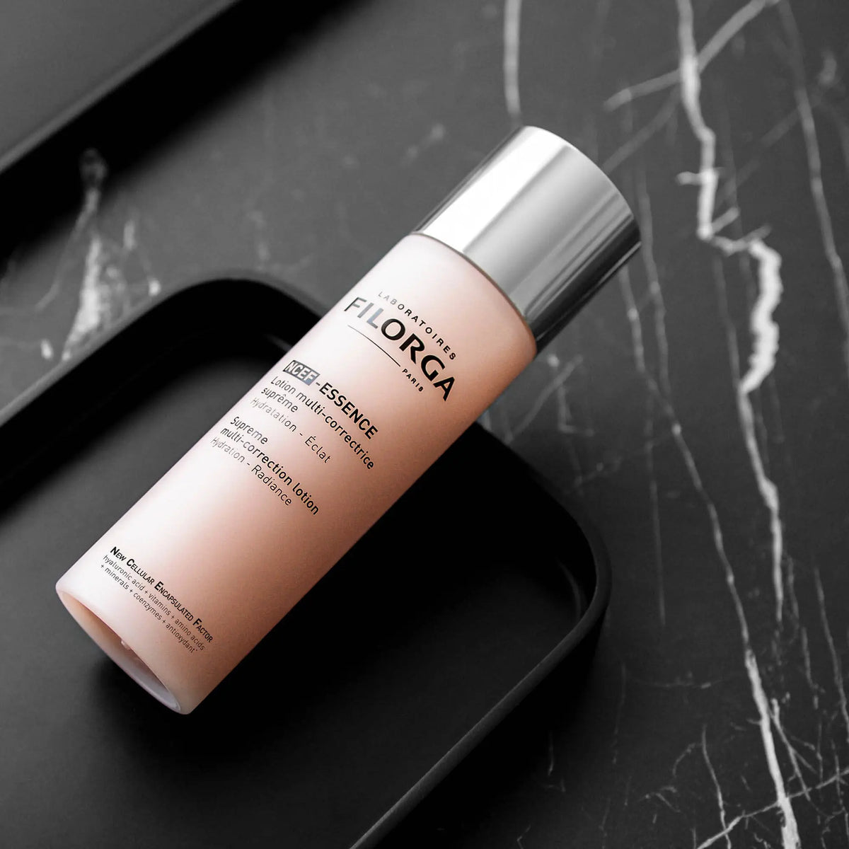 Frasco rosa-claro Filorga NCEF-ESSENCE, loção multicorretora de 150 ml, com tampa prateada.